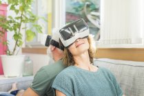Mature couple sitting on couch at home and wearing VR glasses — Stock Photo