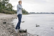 Man talking on mobile phone standing at riverside looking at view — Stock Photo