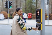Royaume-Uni, Londres, portrait d'une femme souriante appuyant sur le bouton de lumière piétonne — Photo de stock