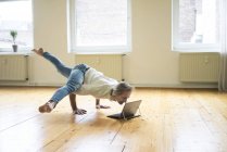 Mature man doing handstand on floor in empty room and looking at tablet — Stock Photo