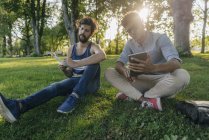Two multicultural friends sitting in park with mobile device and papers — Stock Photo