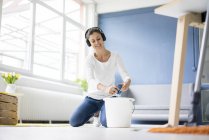 Mujer sonriente en casa usando auriculares y limpiando el piso - foto de stock