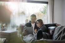 Smiling couple lying on couch at home and sharing tablet — Stock Photo