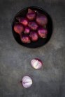 Cebollas rosadas frescas en tazón sobre superficie gris con mitades - foto de stock