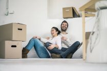 Couple riant assis dans une nouvelle maison entourée de boîtes en carton — Photo de stock