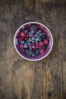 Bowl of deep frozen red currents, raspberries blueberries and blackberries on rustic wooden table — Stock Photo