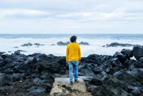 Azores, Sao Miguel, rear view of man looking at the sea from stony coast — Stock Photo