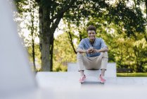 Усміхнений молодий афроамериканський чоловік з мобільним телефоном сидить у скейтпарку — стокове фото