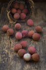 Fresh lychee fruits scattered on rustic wooden table with basket — Stock Photo