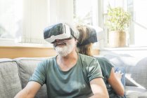 Happy mature couple sitting on couch at home wearing VR glasses — Stock Photo