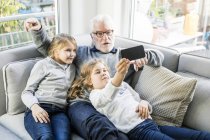 Dos niñas y su abuelo en el sofá tomando una selfie - foto de stock
