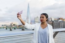 Reino Unido, Londres, mujer parada en un puente tomando una selfie - foto de stock