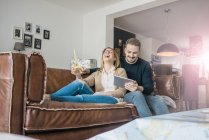 Coppia felice seduta sul divano di casa con tablet e modello Torre Eiffel — Foto stock