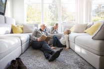 Two girls and grandfather reading book in living room — Stock Photo