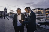 Dois empresários com telemóvel no porto da cidade ao entardecer — Fotografia de Stock