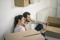 Couple assis dans une nouvelle maison entourée de boîtes en carton regardant tablette — Photo de stock
