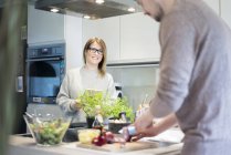 Femme souriante avec tablette regardant petit ami préparer la salade dans la cuisine — Photo de stock