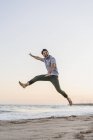 Щасливий молодий чоловік стрибає в повітрі на пляжі на заході сонця — стокове фото