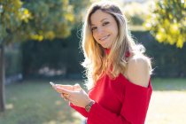 Портрет усміхненої молодої жінки, що використовує смартфон у саду — стокове фото