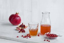 Glass and bottle of pomegranate juice and whole pomegranate and pomegranate seed — Stock Photo