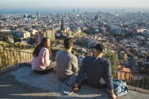 Espanha, Barcelona, três amigos sentados em uma parede com vista para a cidade — Fotografia de Stock