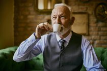 Elegante hombre mayor bebiendo café en un café - foto de stock