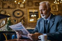 Elegant senior man reading newspaper in a cafe — Stock Photo