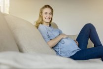 Porträt einer lächelnden Schwangeren, die zu Hause auf dem Sofa sitzt — Stockfoto