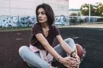 Молодая женщина сидит с баскетбольным мячом на открытой площадке — стоковое фото