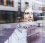 Smiling young woman looking out of window — Stock Photo