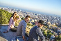 Espanha, Barcelona, três amigos sorridentes sentados em uma parede com vista para a cidade — Fotografia de Stock