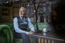 Elégant homme âgé assis sur le canapé dans un café et regardant par la fenêtre — Photo de stock