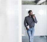 Homme d'affaires heureux debout à vitre et en utilisant smartphone — Stock Photo