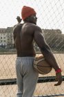 Вид ззаду м'язистого афроамериканського баскетболіста, що стоїть на паркані — стокове фото