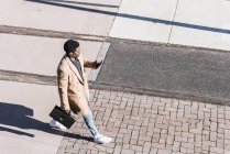 Empresario caminando al aire libre con maletín, teléfono celular y auriculares - foto de stock