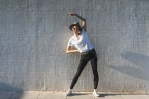 Усміхнена жінка в капелюсі стоїть перед плиткою стіни роблять розтяжки вправи — стокове фото
