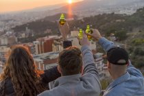 Espanha, Barcelona, três amigos com garrafas de cerveja em uma colina com vista para a cidade ao pôr do sol — Fotografia de Stock