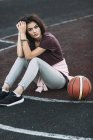Портрет молодой женщины, сидящей с баскетбольным мячом на открытой площадке — стоковое фото