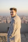 Portrait of smiling young man wearing grey coat at sunset — Stock Photo