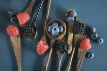 Fresh ripe blueberries, raspberries and blackberries in wooden spoons on dark blue background — Stock Photo