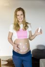 Retrato de una mujer embarazada sonriente aplicando crema en su vientre - foto de stock