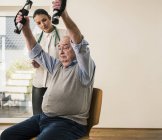 Молодая женщина, поддерживающая старшего мужчину, делая упражнения на руках — стоковое фото