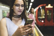 Adolescente utilisant un téléphone portable à la station de métro — Photo de stock