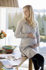 Smiling pregnant woman working at home and sitting on table — Stock Photo