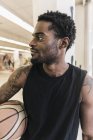 Афроамериканський чоловік з татуюваннями тримає баскетбольний м'яч і дивиться геть — стокове фото