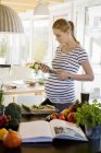 Pregnant woman in kitchen at home using tablet — Stock Photo
