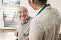 Senior man smiling at nurse at home — Stock Photo