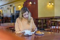 Young woman in a cafe with notebook, pastry and coffee — Stock Photo
