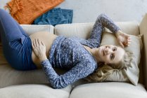 Portrait de femme enceinte heureuse allongée sur le canapé à la maison — Photo de stock