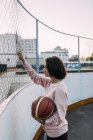 Молодая женщина, стоящая с баскетбольным мячом возле забора — стоковое фото